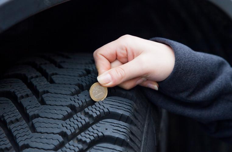 Main avec pièce de monnaie pour mesurer la profondeur de profil d'un pneu