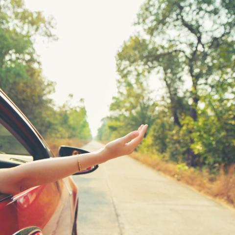 vrouw steekt hand uit wagen op weg